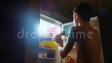 小男孩晚上从冰箱里吃饥饿和饕餮。 青少年男孩晚上看冰箱的生活方式